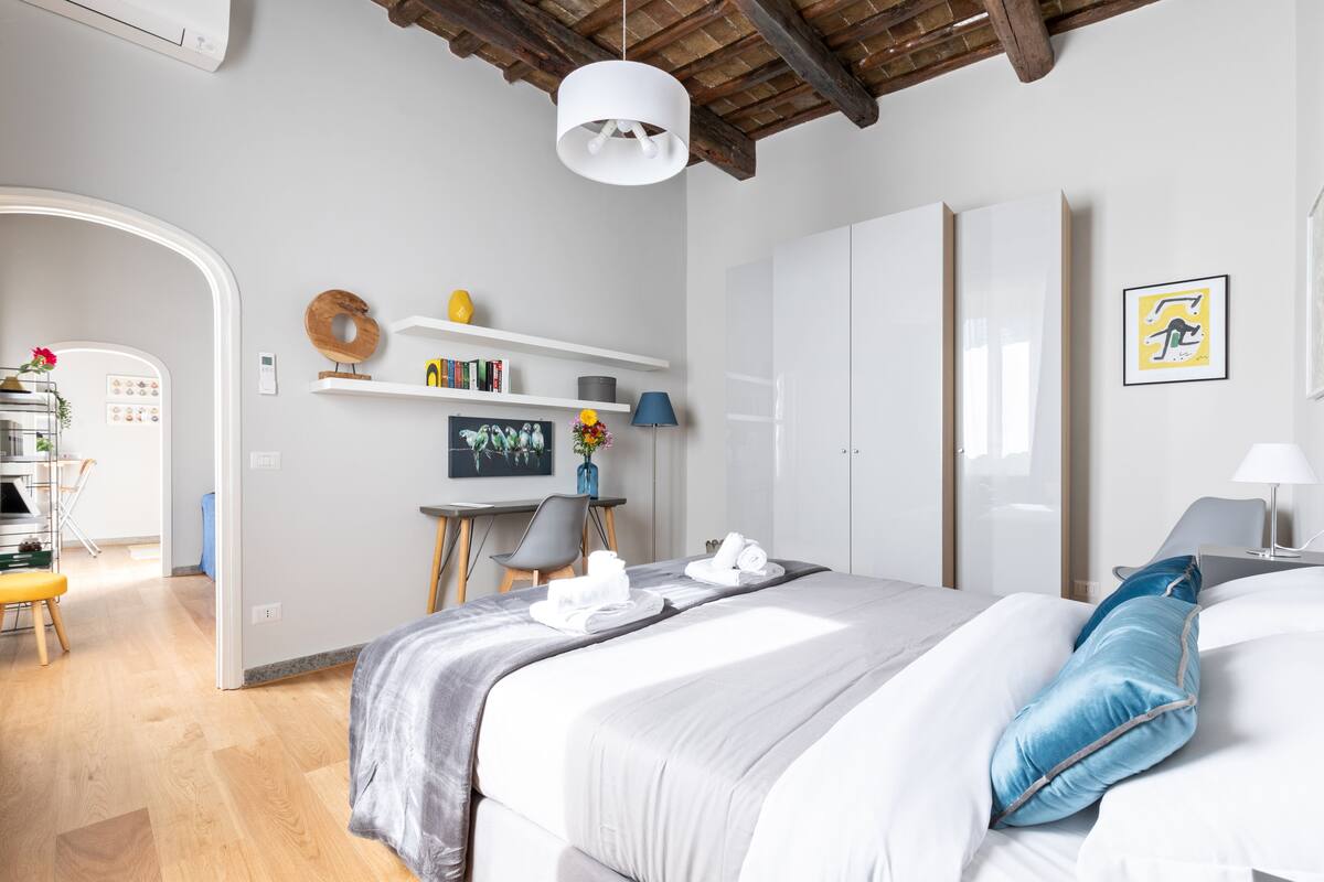 A modern hotel room with a bed, a desk, and a wardrobe.