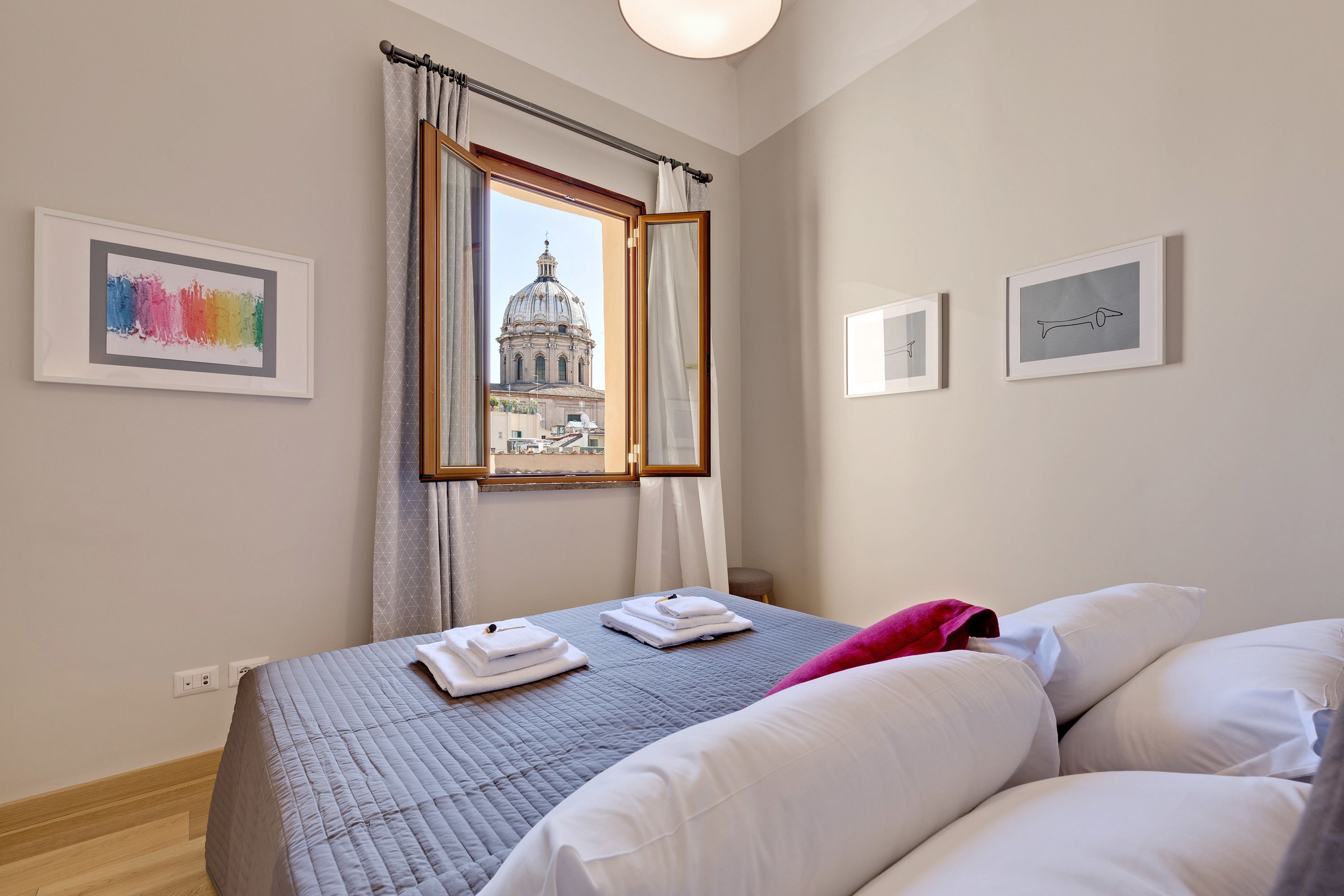 A hotel room with a bed, a window with a view of a dome-shaped building, and framed artwork on the walls.