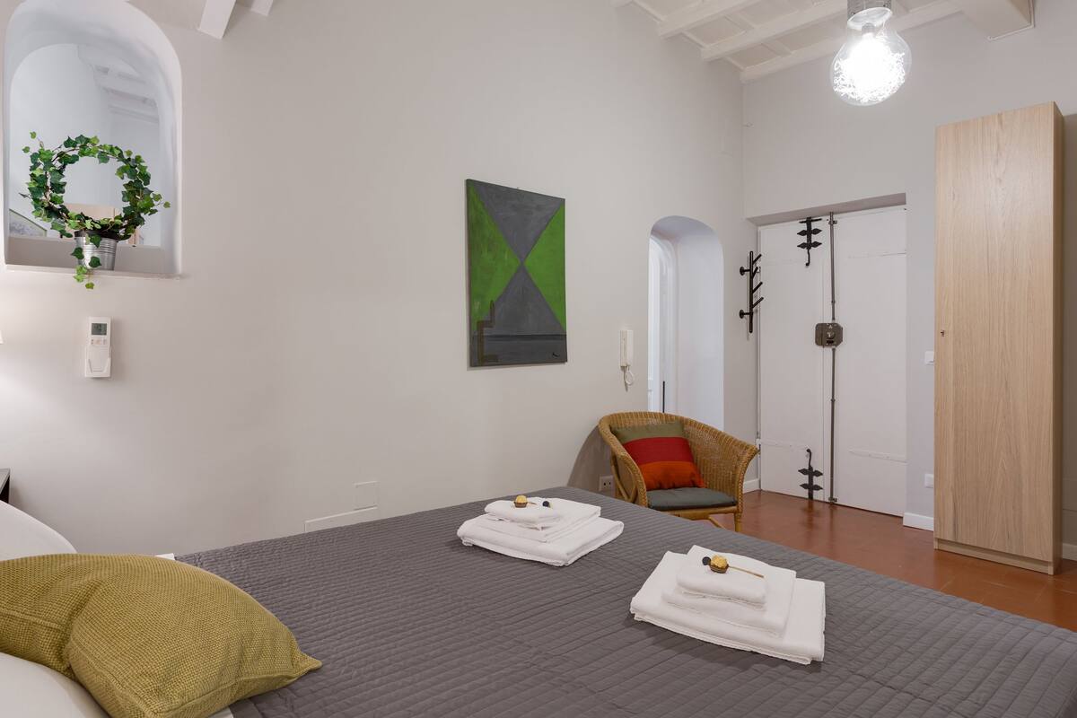A hotel room with a bed, a chair, a wardrobe, and a painting on the wall.