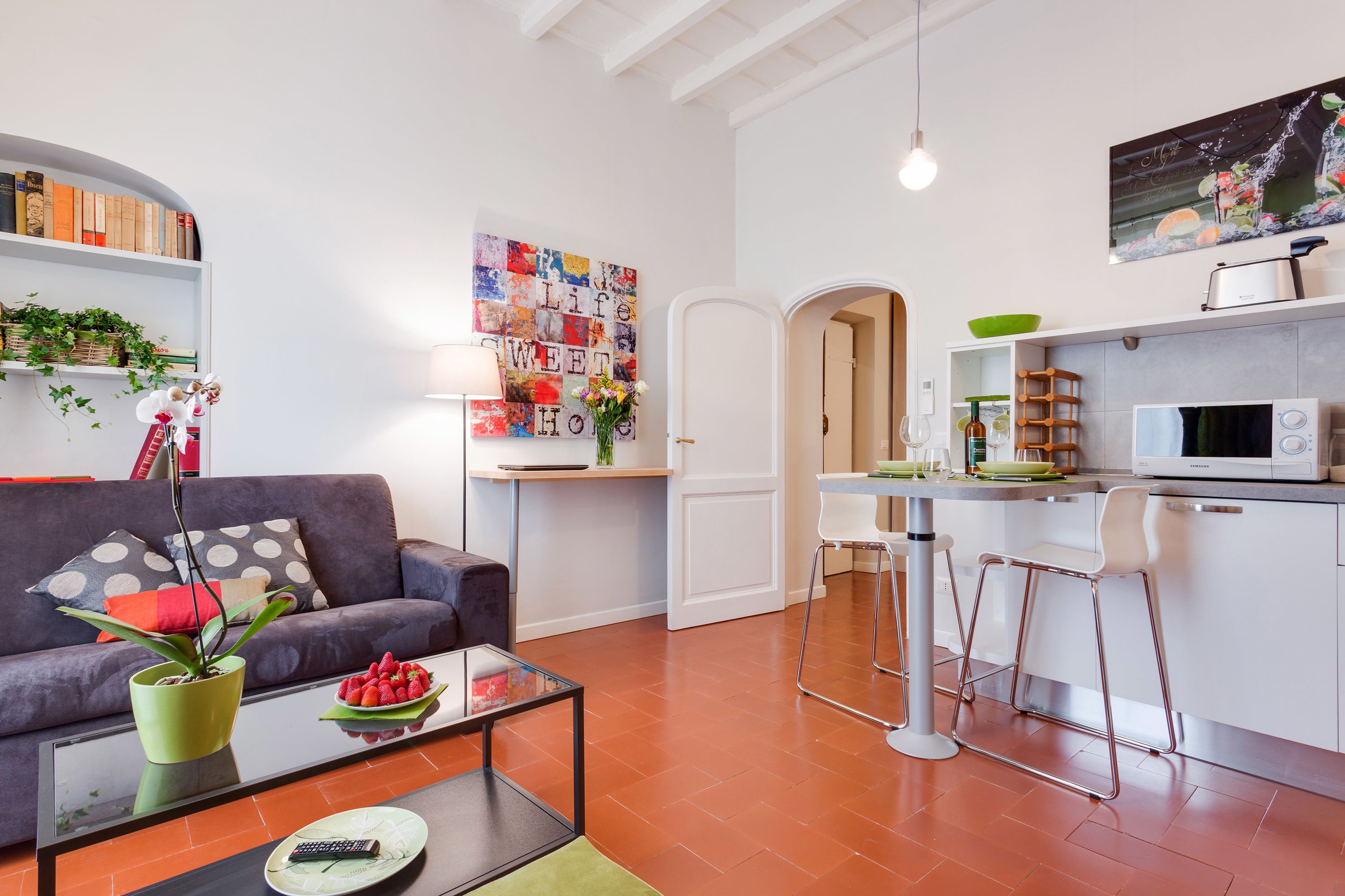 Una sala de estar moderna con un sofá, una mesa de centro y una zona de cocina con microondas y taburetes de bar.
