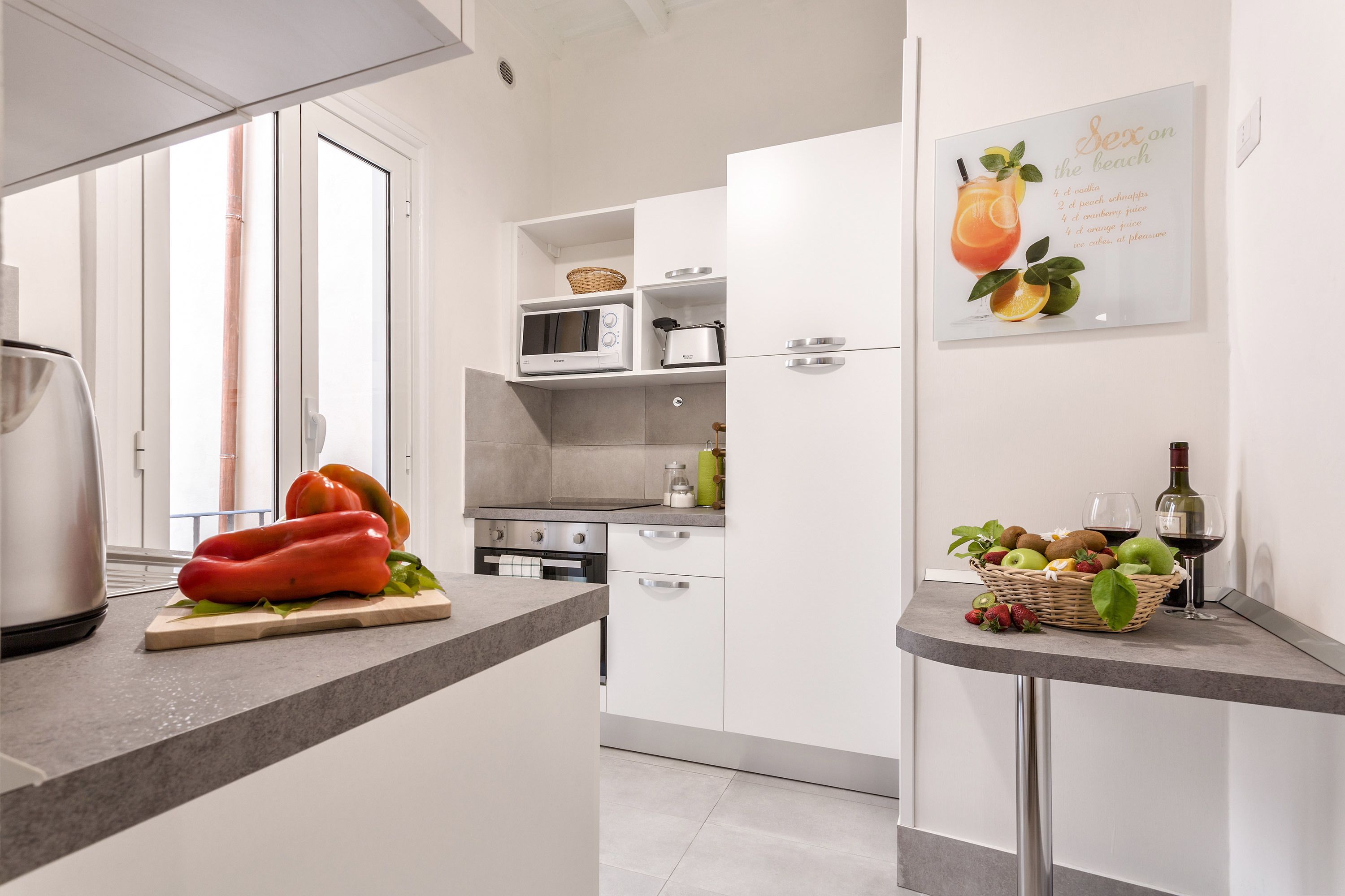 A modern kitchen with white cabinets, a microwave, a toaster, and a fruit basket on the counter.