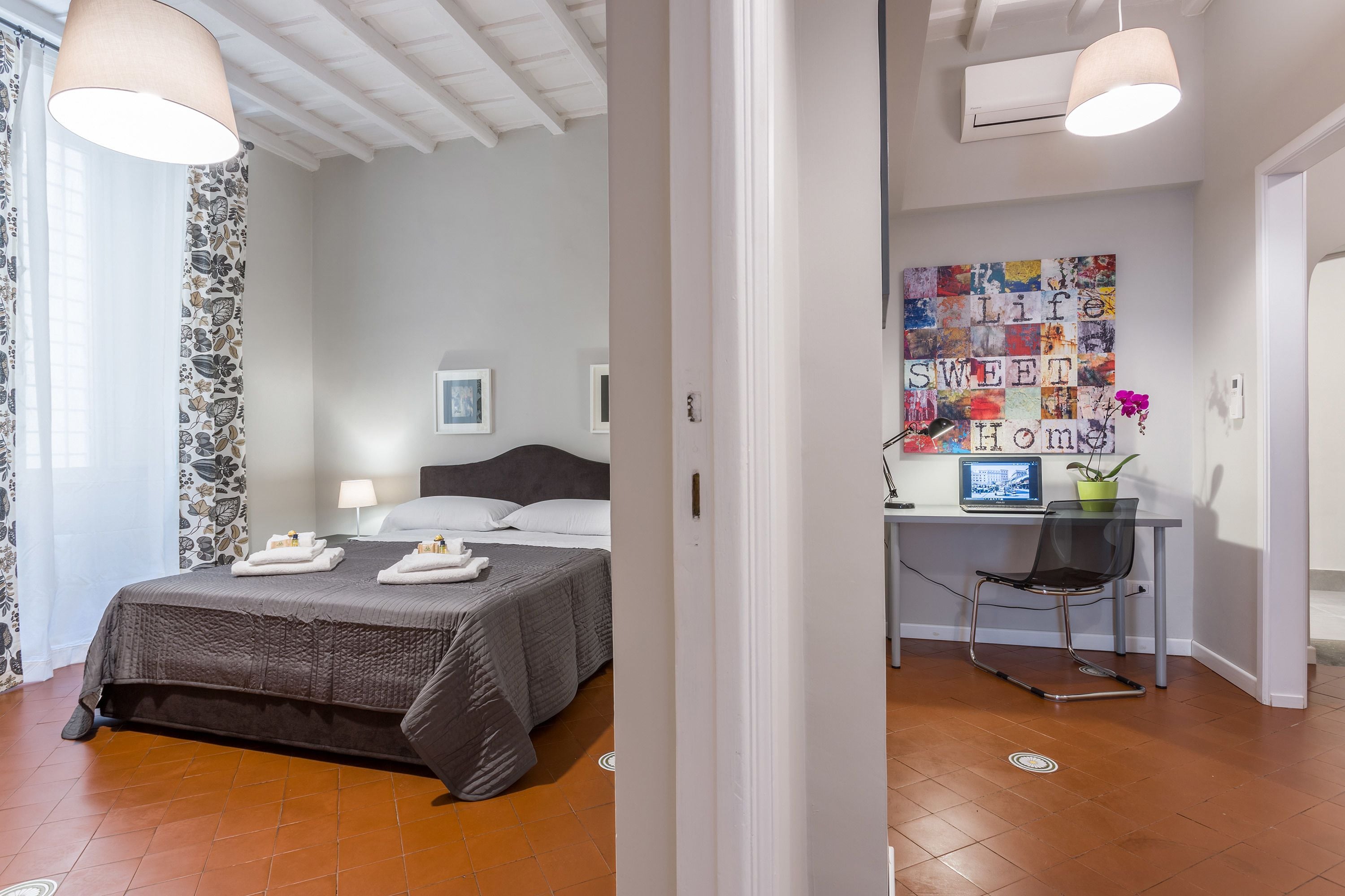 A modern bedroom with a large bed, a desk with a computer, and a wall art piece.