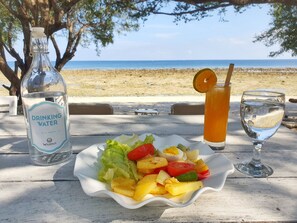 A table with a bottle of drinking water, a glass of iced tea, and a plate of fruit salad. - Wilsons Retreat (Gili Trawangan)