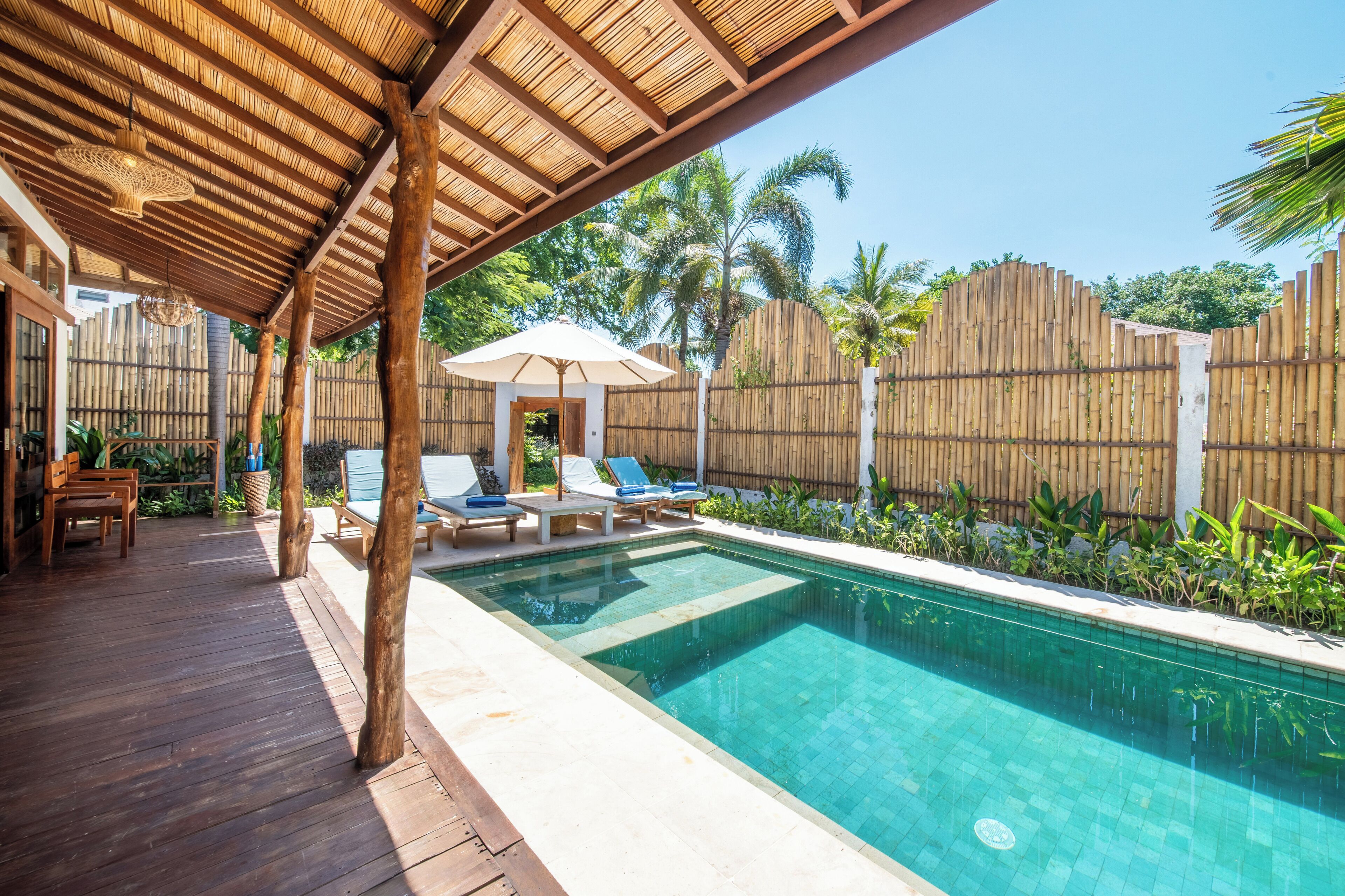 Zona de piscina con terraza de madera, sillas de descanso y un área de estar cubierta.
