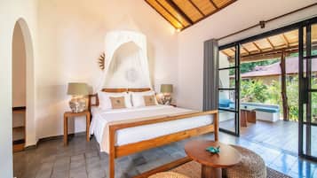 A bedroom with a wooden bed, two bedside tables with lamps, a large window, and a balcony with a view of greenery.