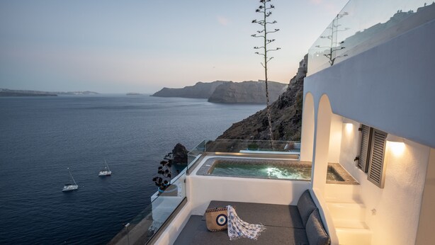 Un balcón con vistas al mar, un jacuzzi y una zona de estar con cojines y una toalla.