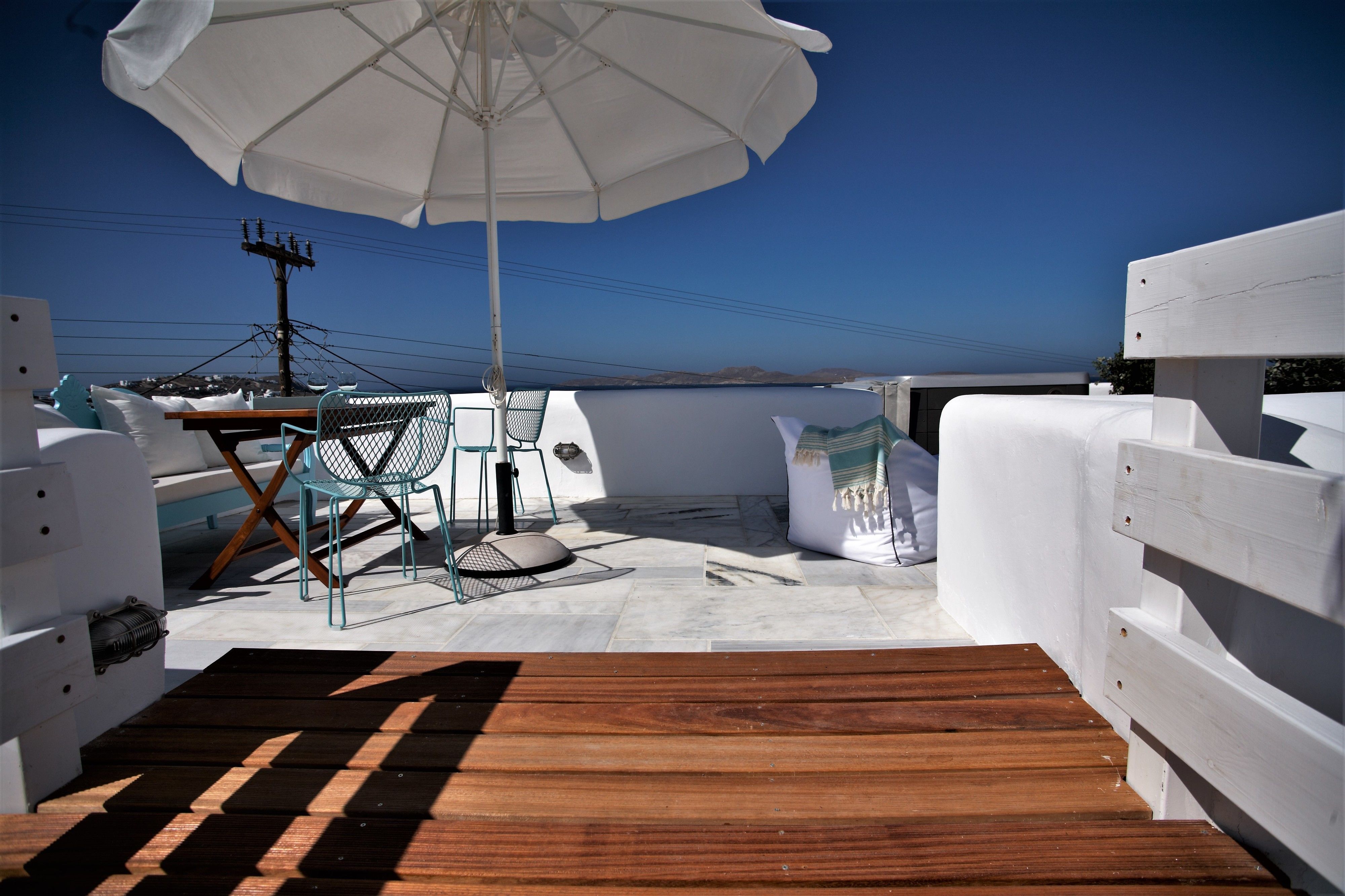 Een terras met houten vloer, witte zachte zitplaatsen, een tafel en een parasol.