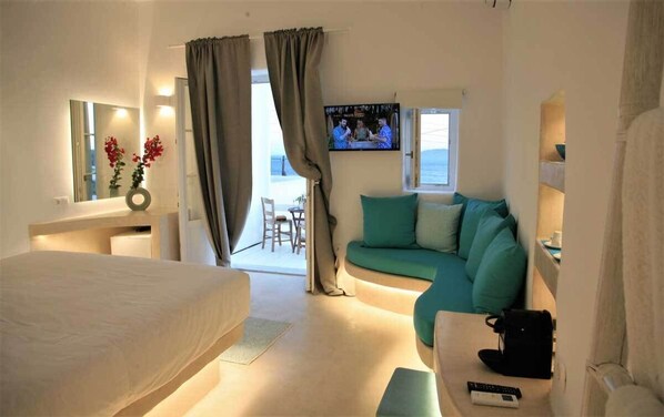 A hotel room with a bed, a sofa, a TV, and a view of the sea. - Mykonos Moussa Suites (Mykonos)