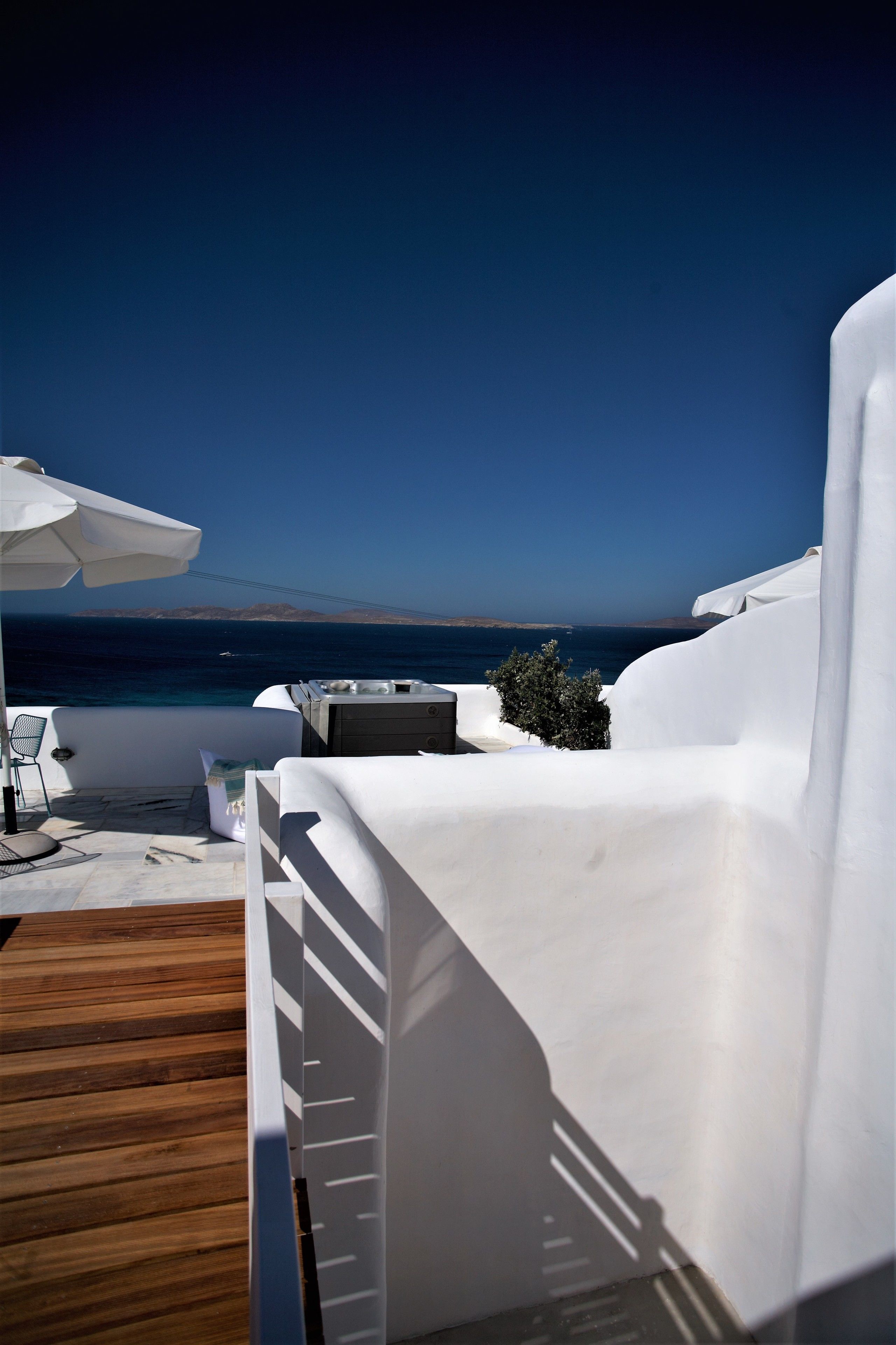 Un espacio al aire libre con asientos blancos, una terraza de madera, una sombrilla blanca y vista al mar.