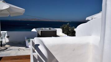 Un espacio al aire libre con asientos blancos, una terraza de madera, una sombrilla blanca y vista al mar.