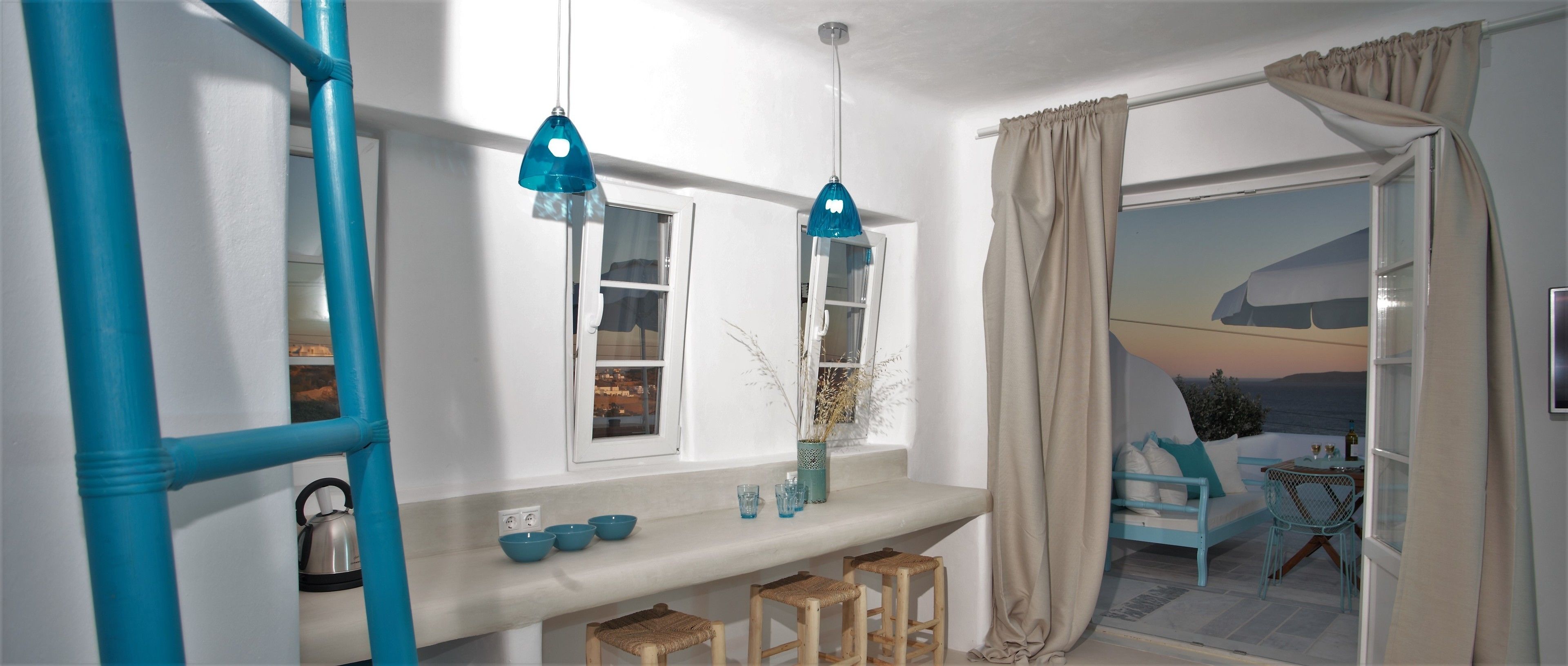 A room with a white wall, a window with a view, a blue pendant light, a table with a vase, and a chair.