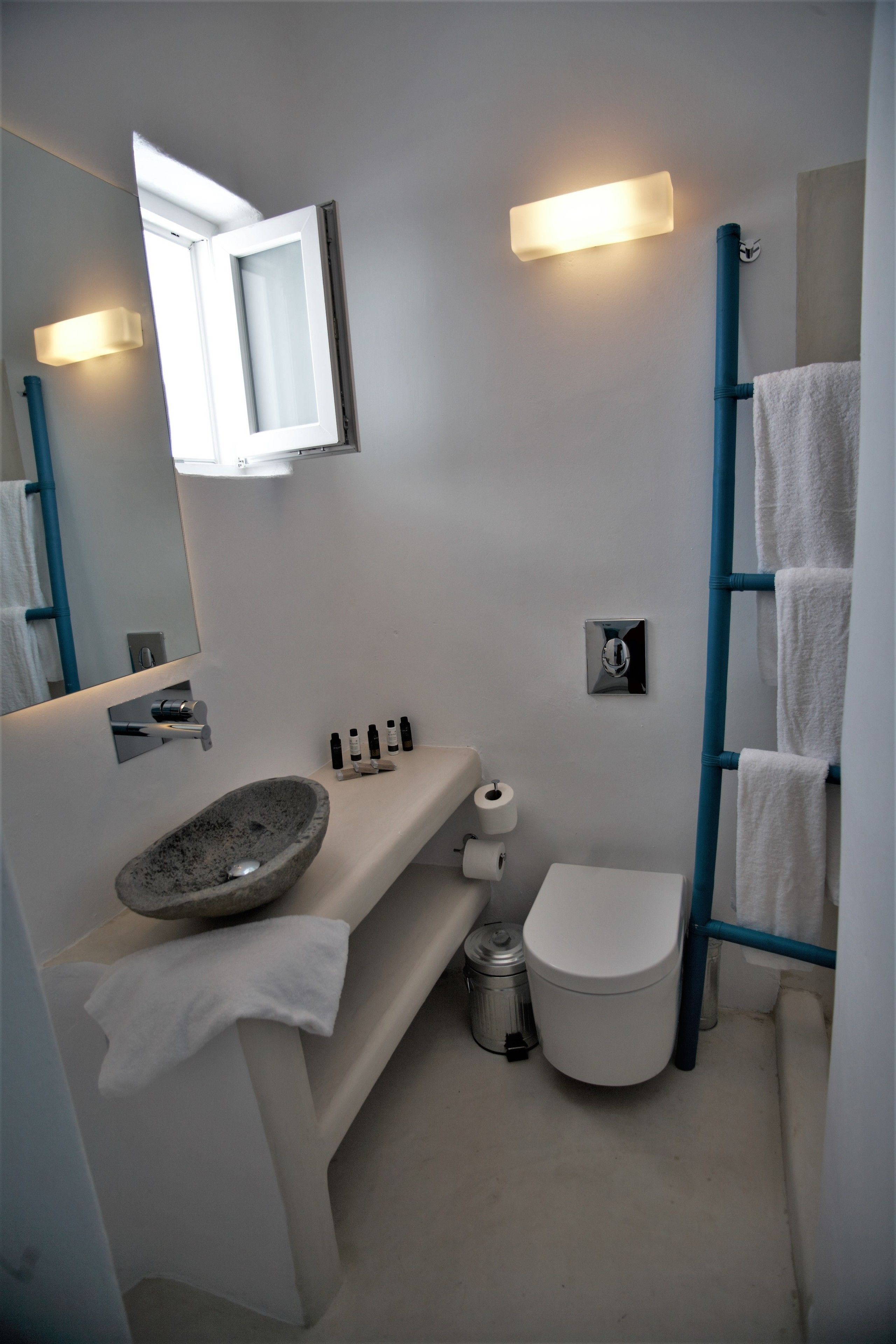Un baño pequeño con un lavabo de piedra, un inodoro, un lavamanos con espejo y un perchero para toallas.