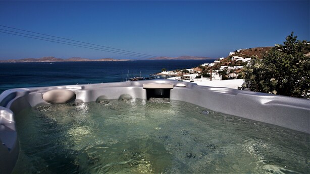 A hot tub with clear water, surrounded by white buildings and a view of the sea and distant hills. - Mykonos Moussa Suites (Mykonos)
