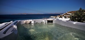 A hot tub with clear water, surrounded by white buildings and a view of the sea and distant hills. - Mykonos Moussa Suites (Mykonos)