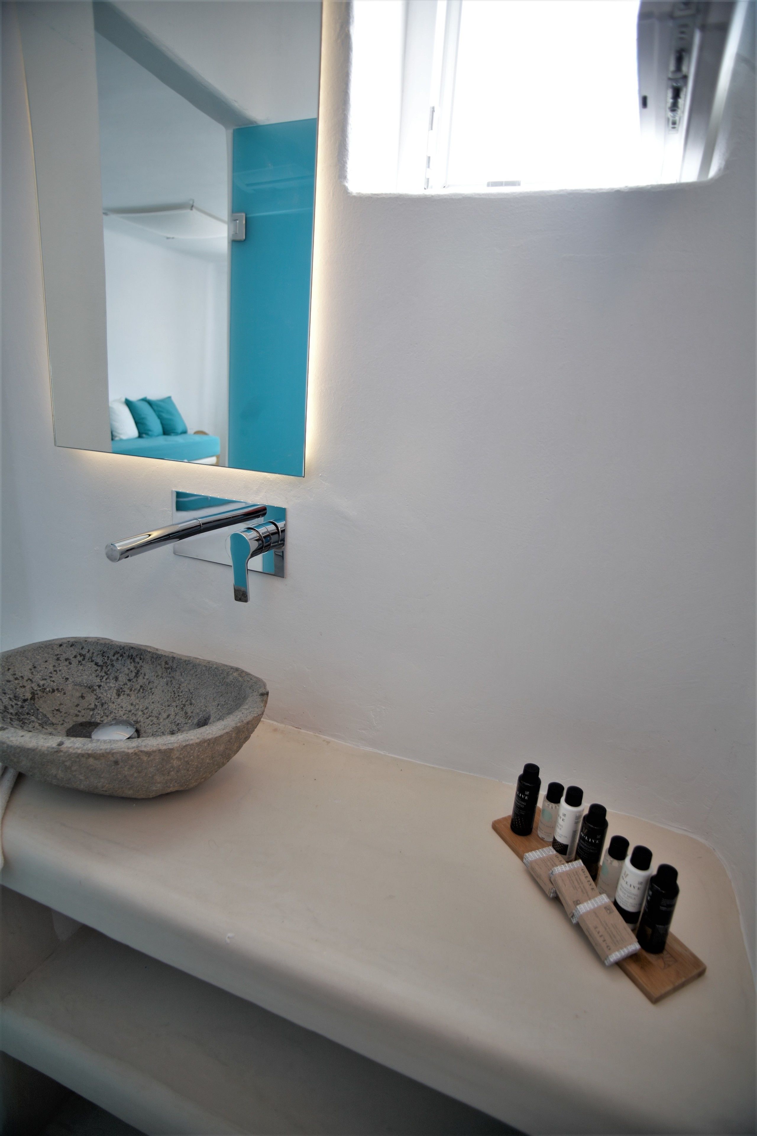 A bathroom with a stone sink, a mirror, and a shelf with toiletries.