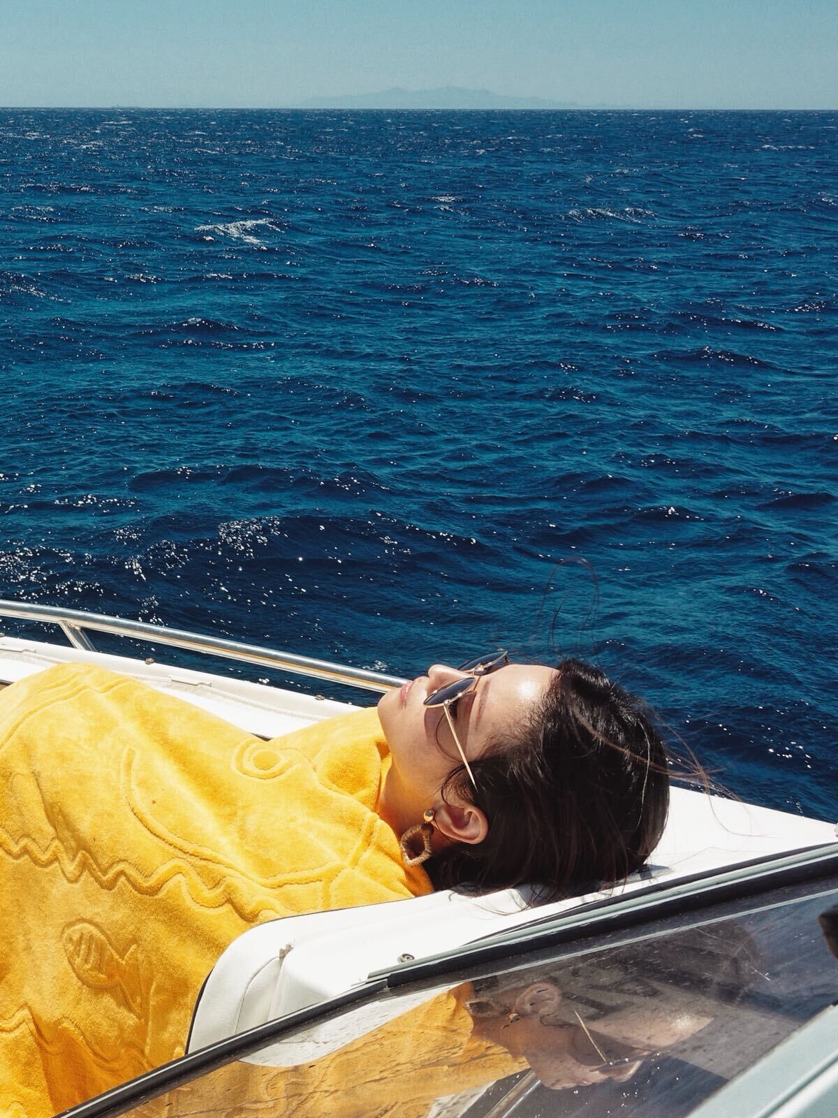 A person lying on a boat with a yellow towel, facing the sea.