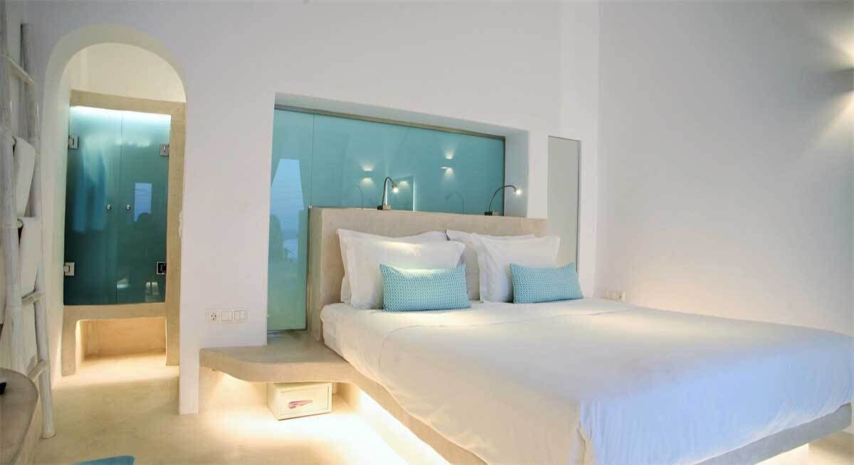 A modern bedroom with a large bed, a built-in headboard, and a glass door leading to a bathroom.