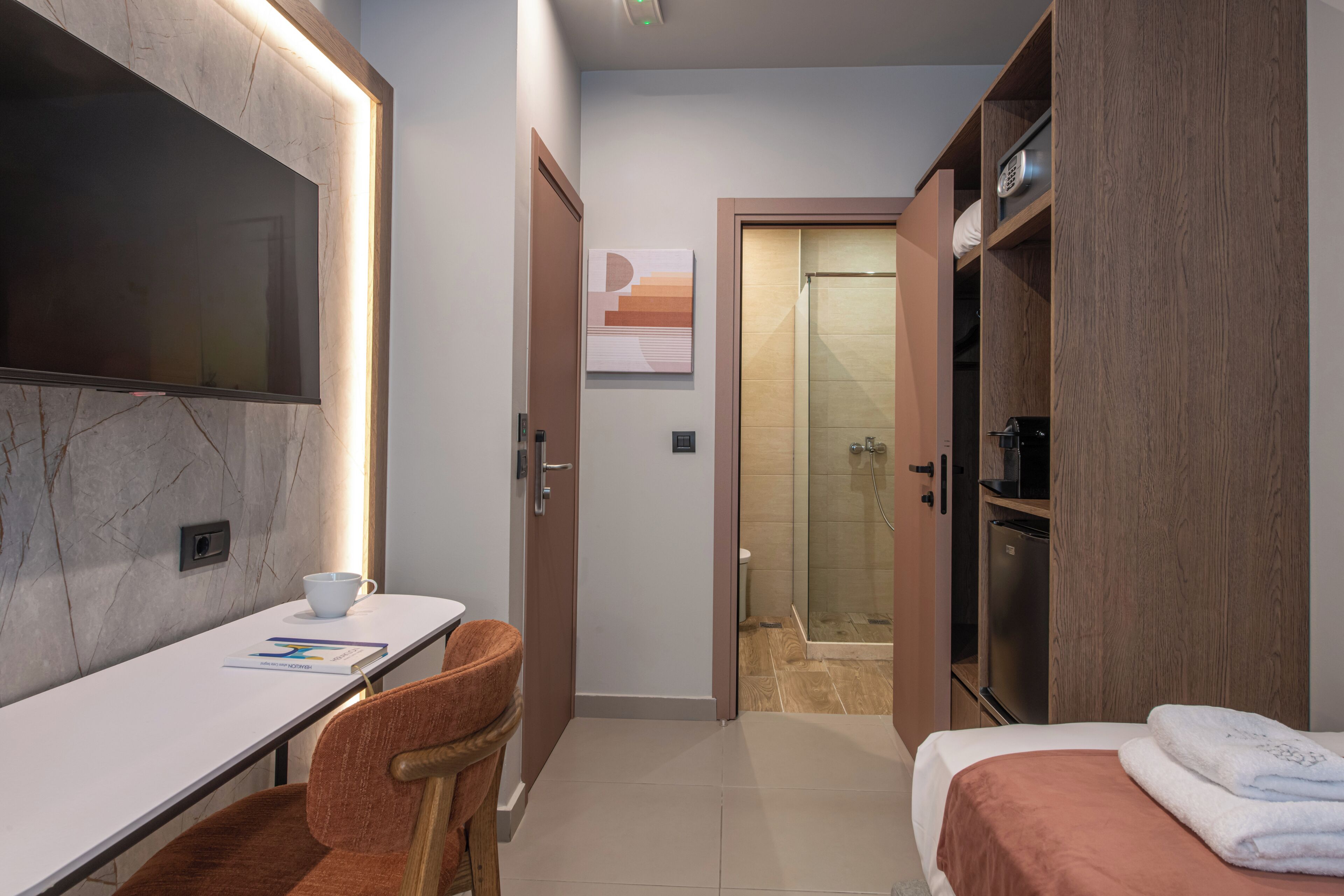 Une chambre d’hôtel comprenant un lit, un bureau avec une chaise, une télévision, un espace douche et une armoire.