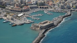 Vista aérea de una ciudad costera con una fortaleza histórica, un puerto deportivo con numerosos barcos y edificios urbanos densos.
