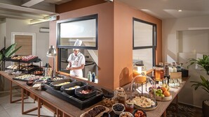 Montaje de bufé con diferentes opciones de comida, un chef preparando alimentos y una cocina al fondo.