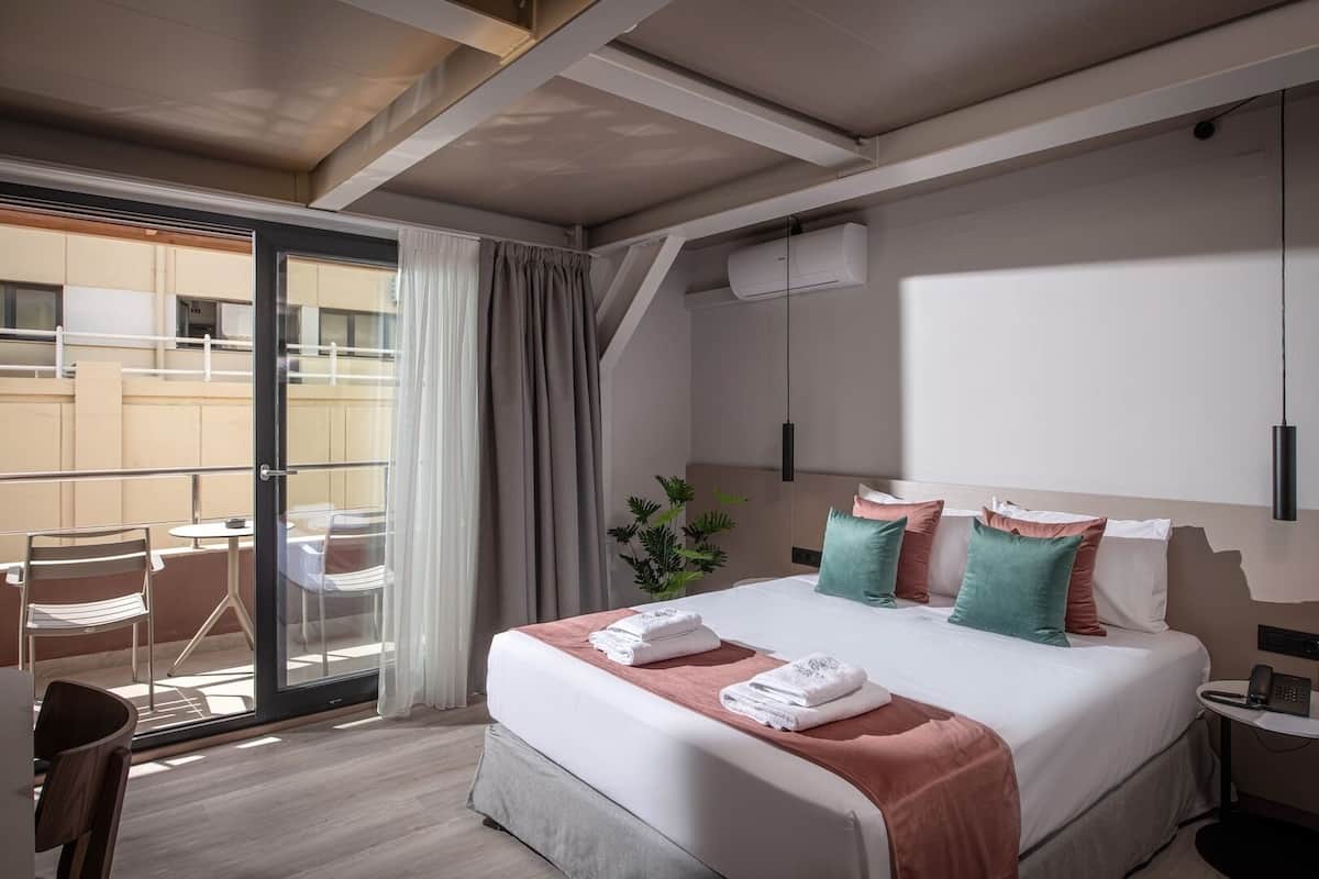 Habitación de hotel con cama, escritorio, silla, balcón y aire acondicionado.