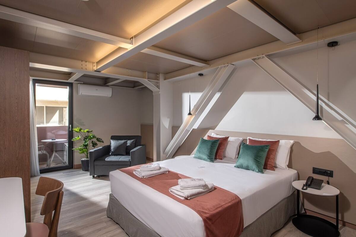 Una habitación de hotel moderna con una cama grande, un escritorio, una silla y vistas al exterior.
