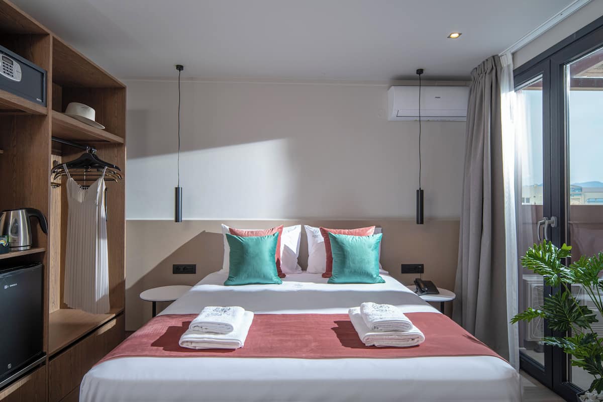 Habitación de hotel con cama, escritorio, silla, mesita, planta y ventana.