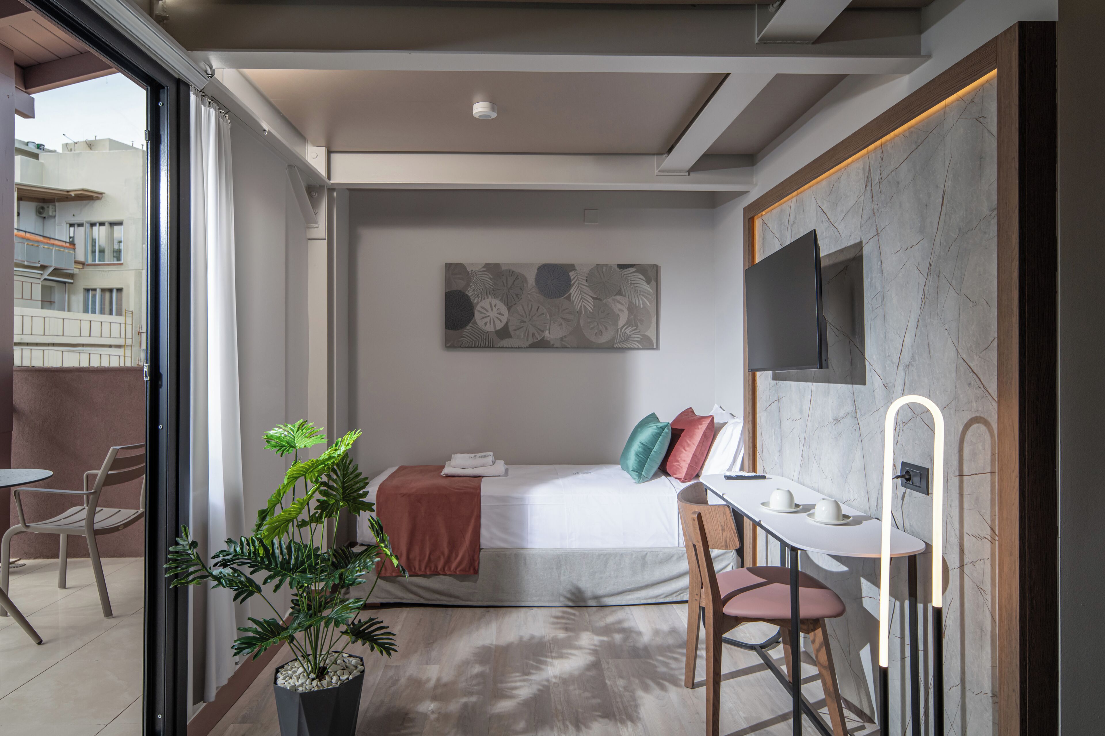 Et moderne hotelværelse med en seng, et skrivebord, en stol, en potteplante og et stort vindue.