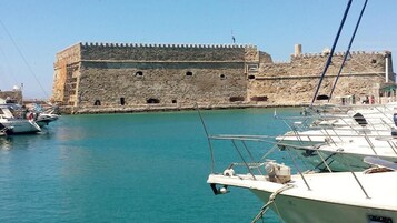 Una fortaleza de piedra histórica junto a un puerto tranquilo con barcos amarrados cerca.
