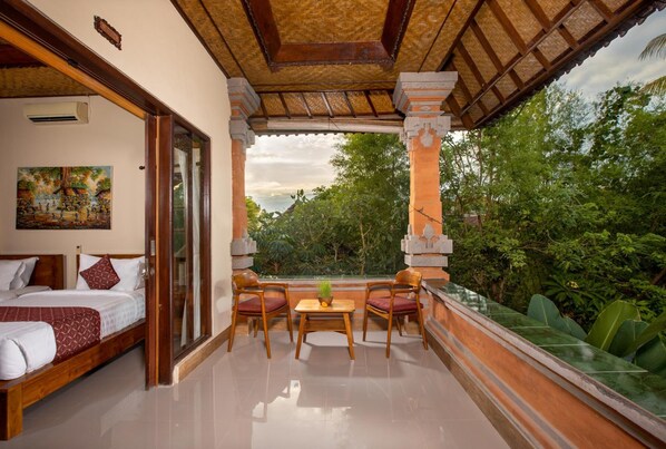 A hotel room with a balcony, a bed, a table with chairs, and a view of greenery.