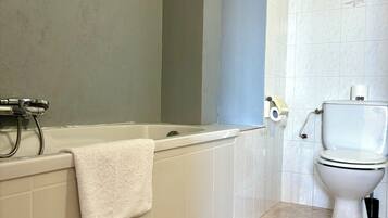 A bathroom with a bathtub, toilet, and tiled floor.