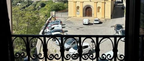 A view of a church with a bell tower, surrounded by parked cars and a hillside with buildings.