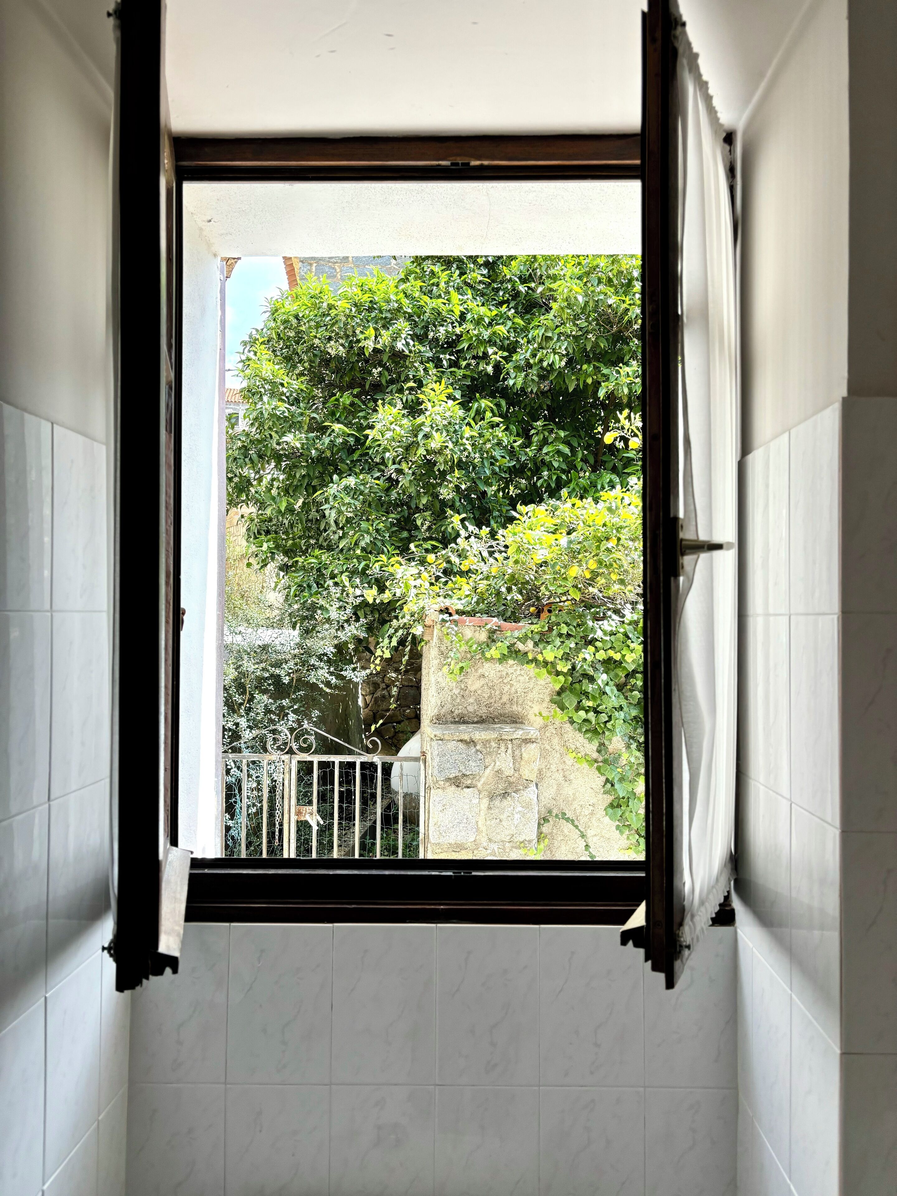 Un baño con ventana, paredes cubiertas de azulejos blancos y una pared de piedra a la vista.