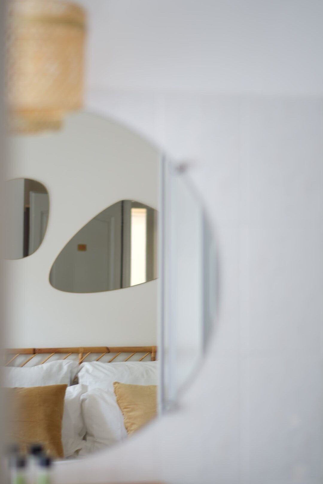 A bedroom with a bed, pillows, and a mirror reflecting part of the room.