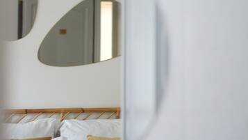 A bedroom with a bed, pillows, and a mirror reflecting part of the room.