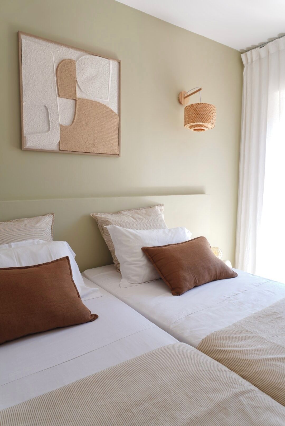 Habitación de hotel con dos camas, una obra de arte en la pared, una lámpara de fibra y una ventana con cortinas blancas.