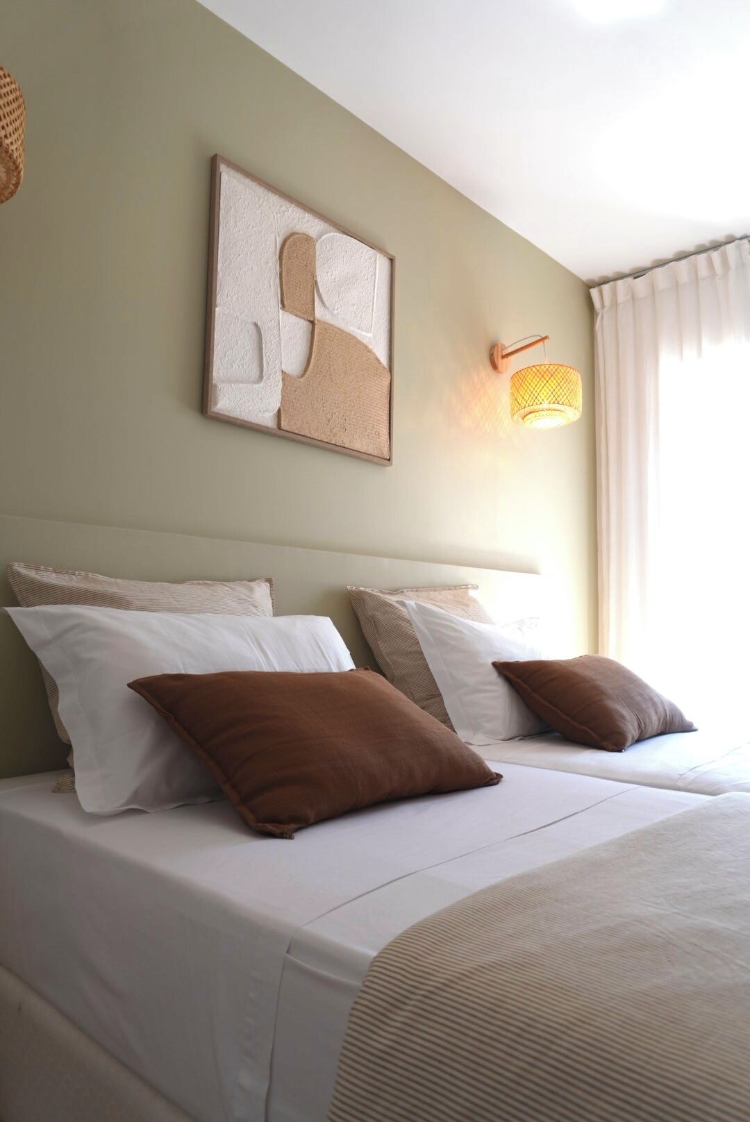 Une chambre d’hôtel avec deux lits, une œuvre d’art accrochée au mur et une lampe fixée au mur.