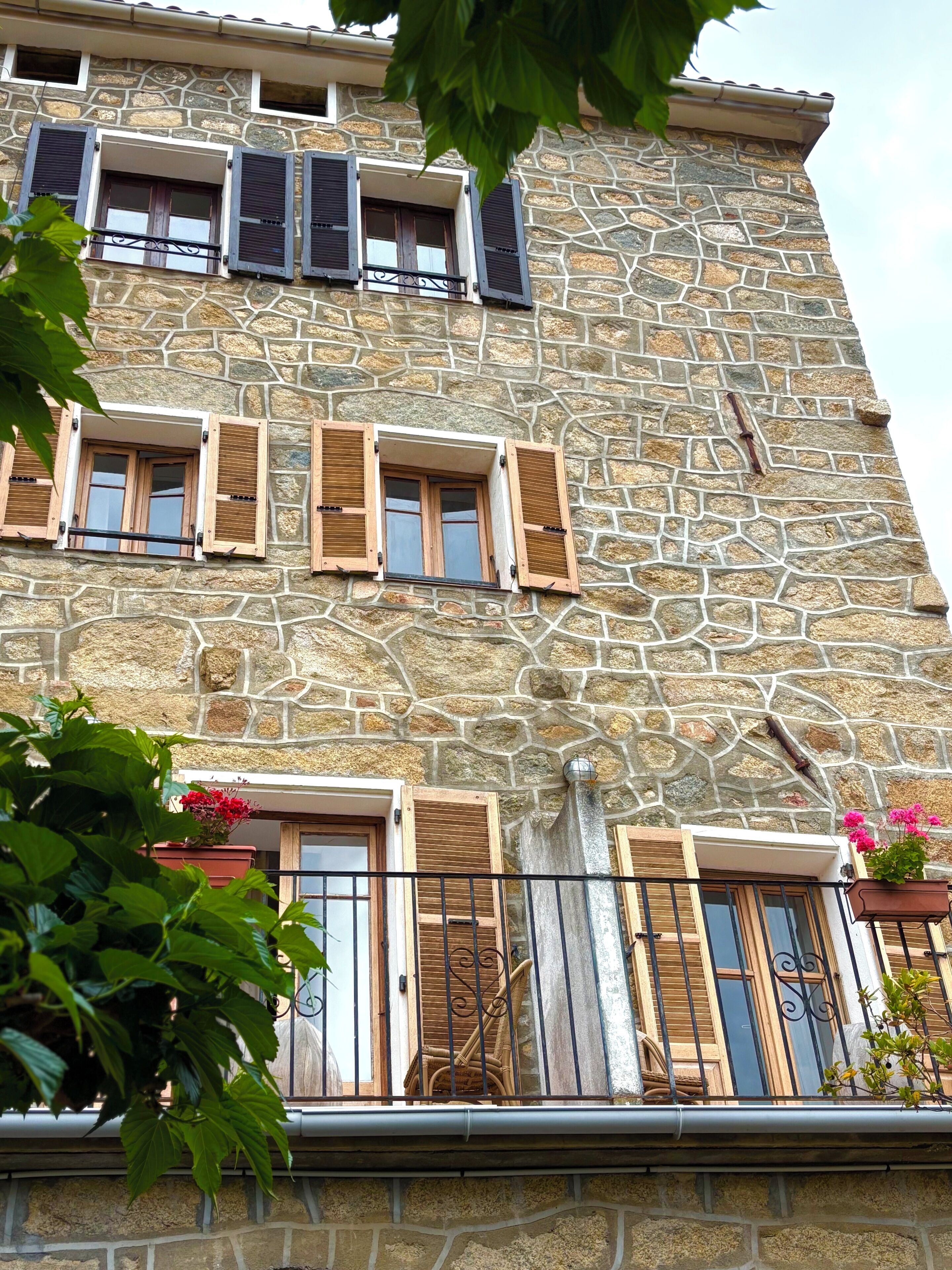 Un edifici de diverses plantes amb façana de pedra, diverses finestres amb persianes i balcons.