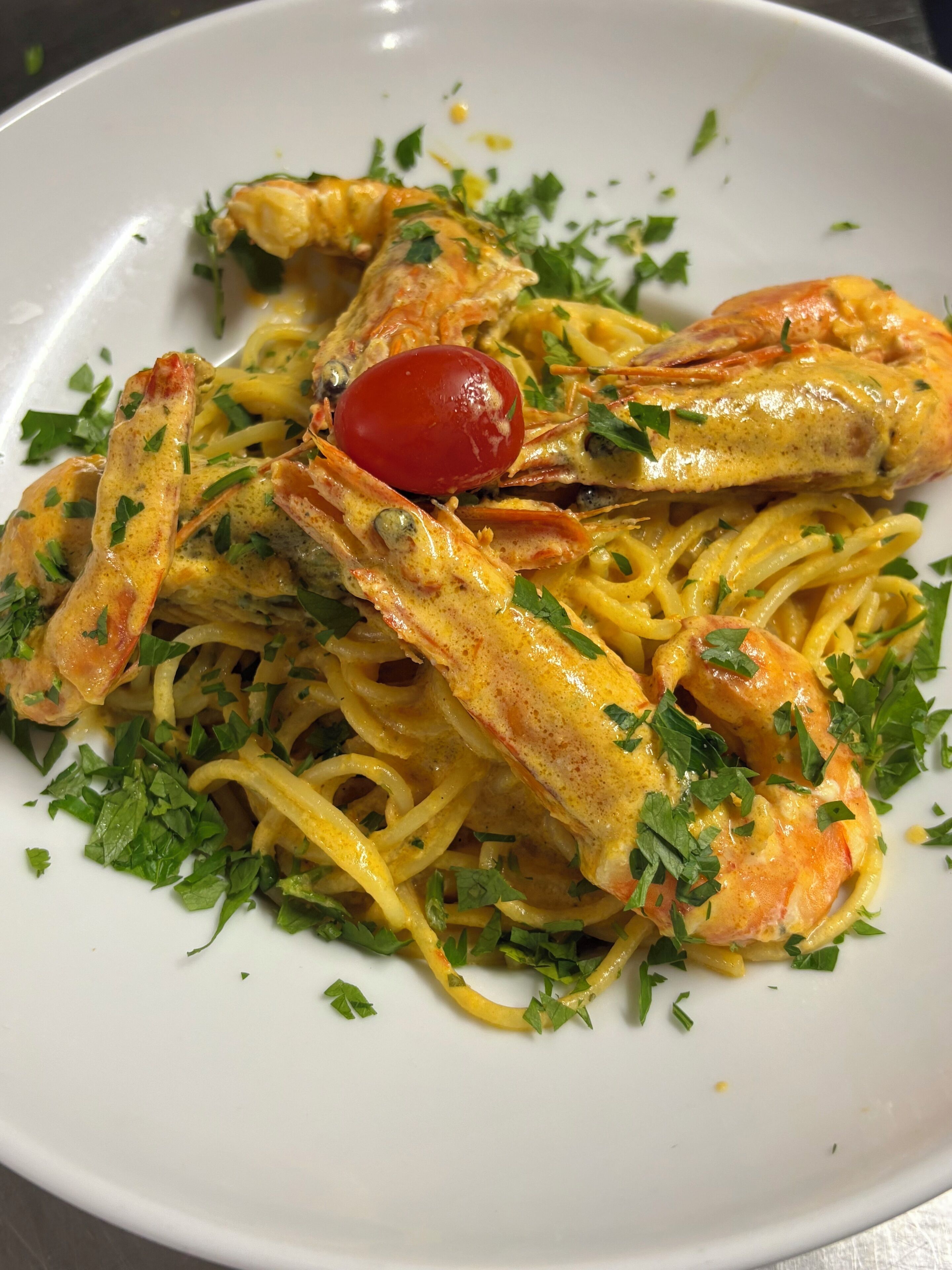 A plate of pasta with shrimp and a cherry tomato garnish.