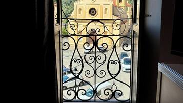 A view through a door with a wrought iron gate, leading to a street with parked cars and a church with a bell tower.