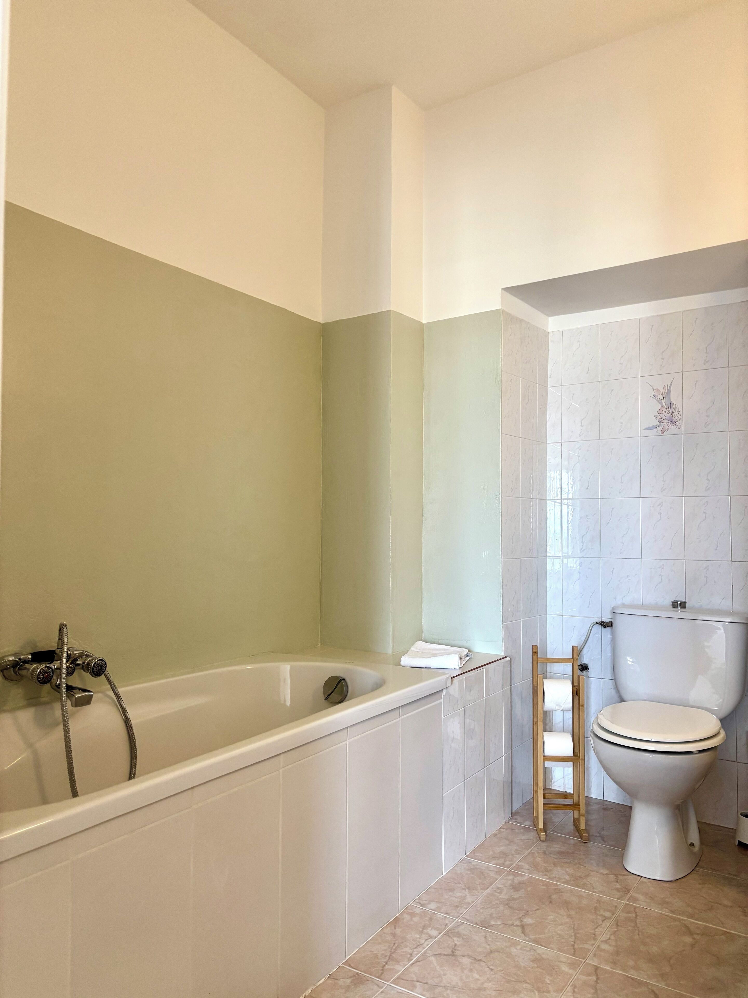 Un baño con bañera, inodoro y un taburete de madera.