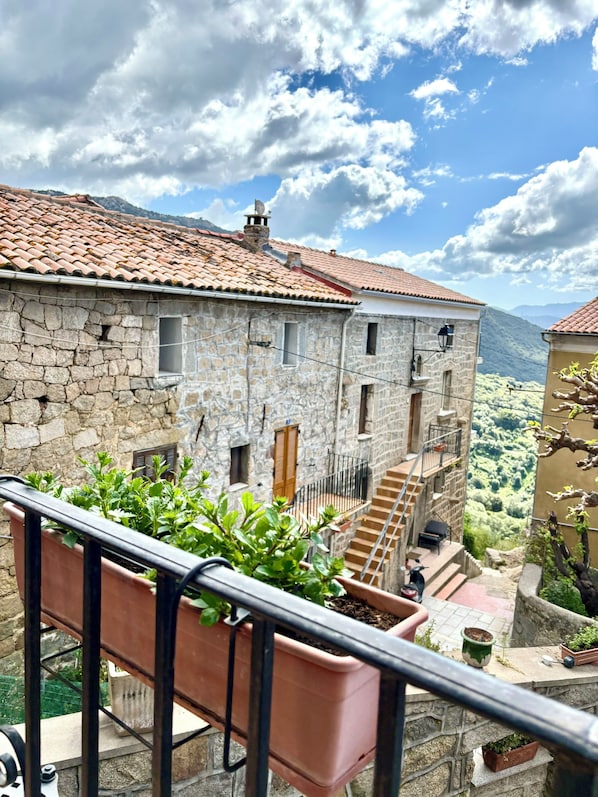 A stone building with a tiled roof, a staircase, and potted plants on a balcony. - Hôtel Restaurant U Santa Maria (Olmeto)
