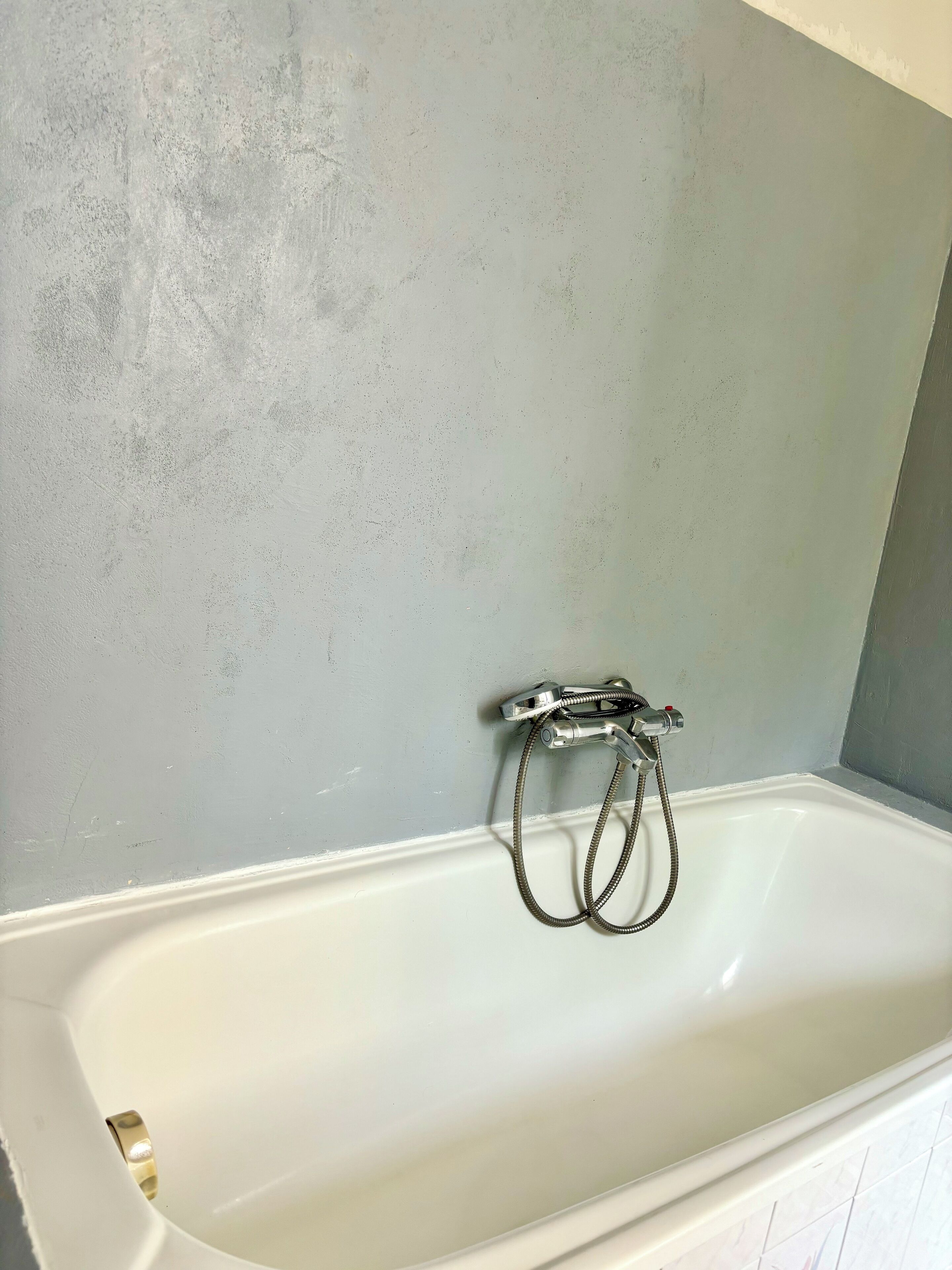 A bathtub with a shower hose, a white bathtub, and a textured wall.
