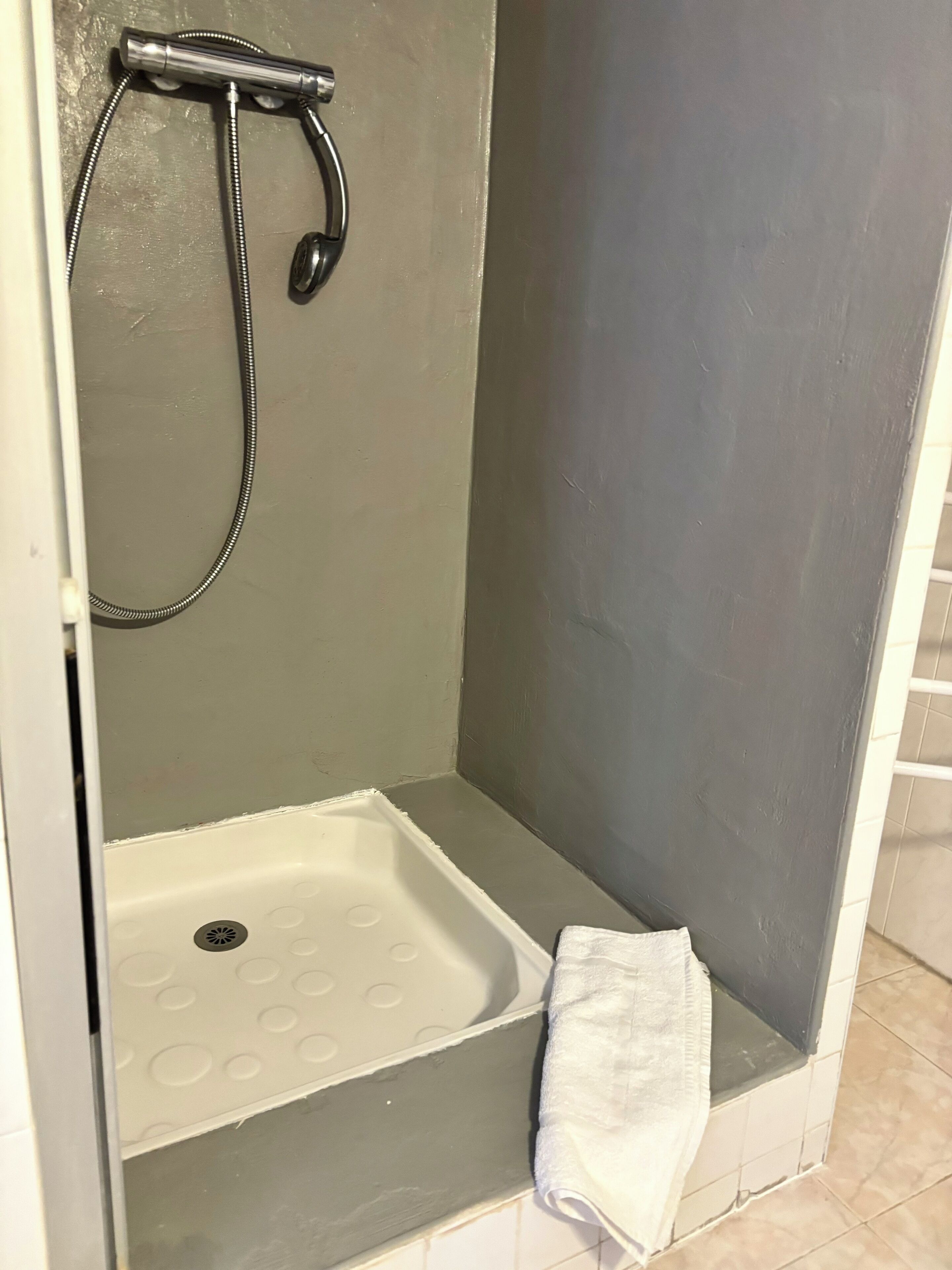 A small, enclosed shower area with a showerhead and a white towel on the floor.