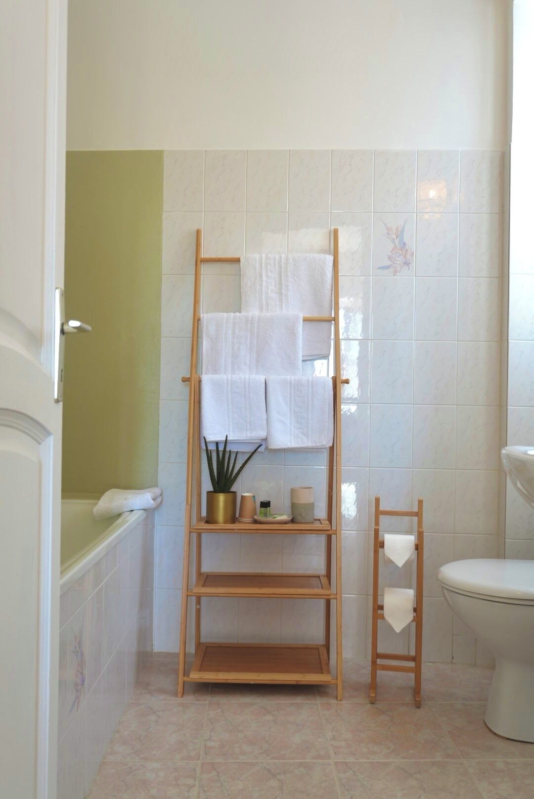 A bathroom with a wooden towel rack holding multiple white towels, a small shelf with toiletries, and a toilet.
