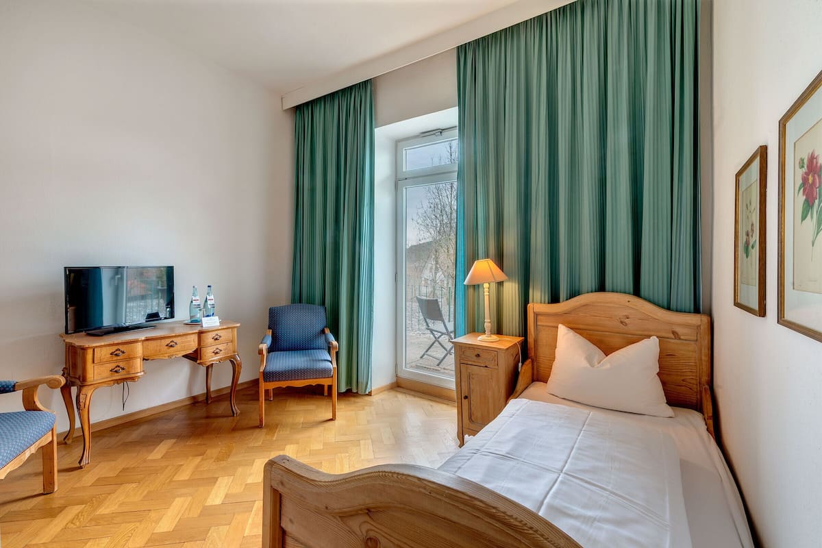 Ein Hotelzimmer mit einem hölzernen Bett, einem Schreibtisch mit Fernseher, einem Sessel und einem Fenster mit Vorhängen.