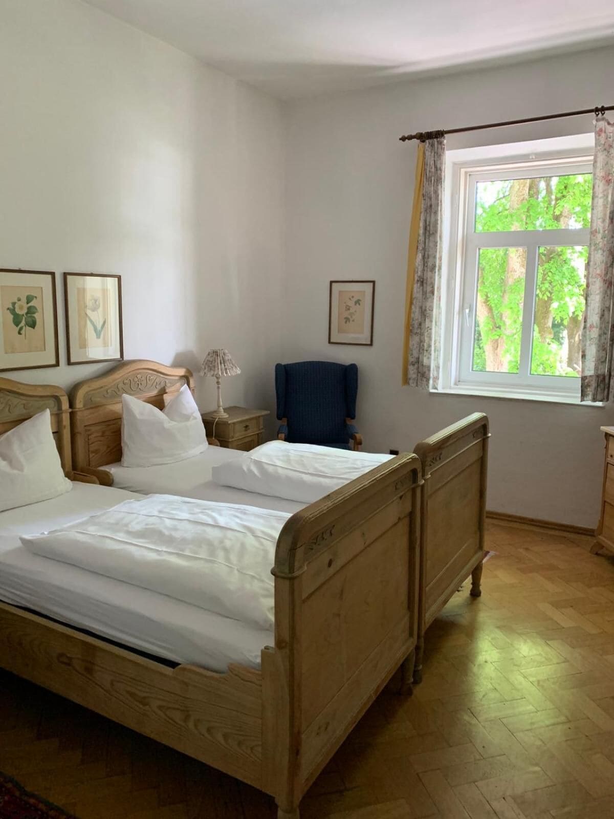 A bedroom with a wooden bed, a chair, a nightstand, and a window with curtains.