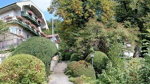 Un sendero conduce a un edificio con fachada curva y balcones decorados con flores.