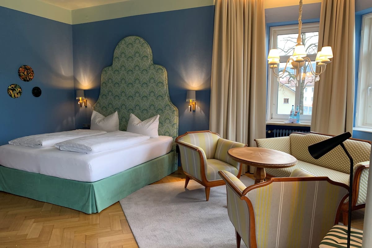 Ein Hotelzimmer mit einem Bett, zwei Sesseln, einer Couch, einem kleinen runden Tisch und einem Fenster mit Vorhängen.
