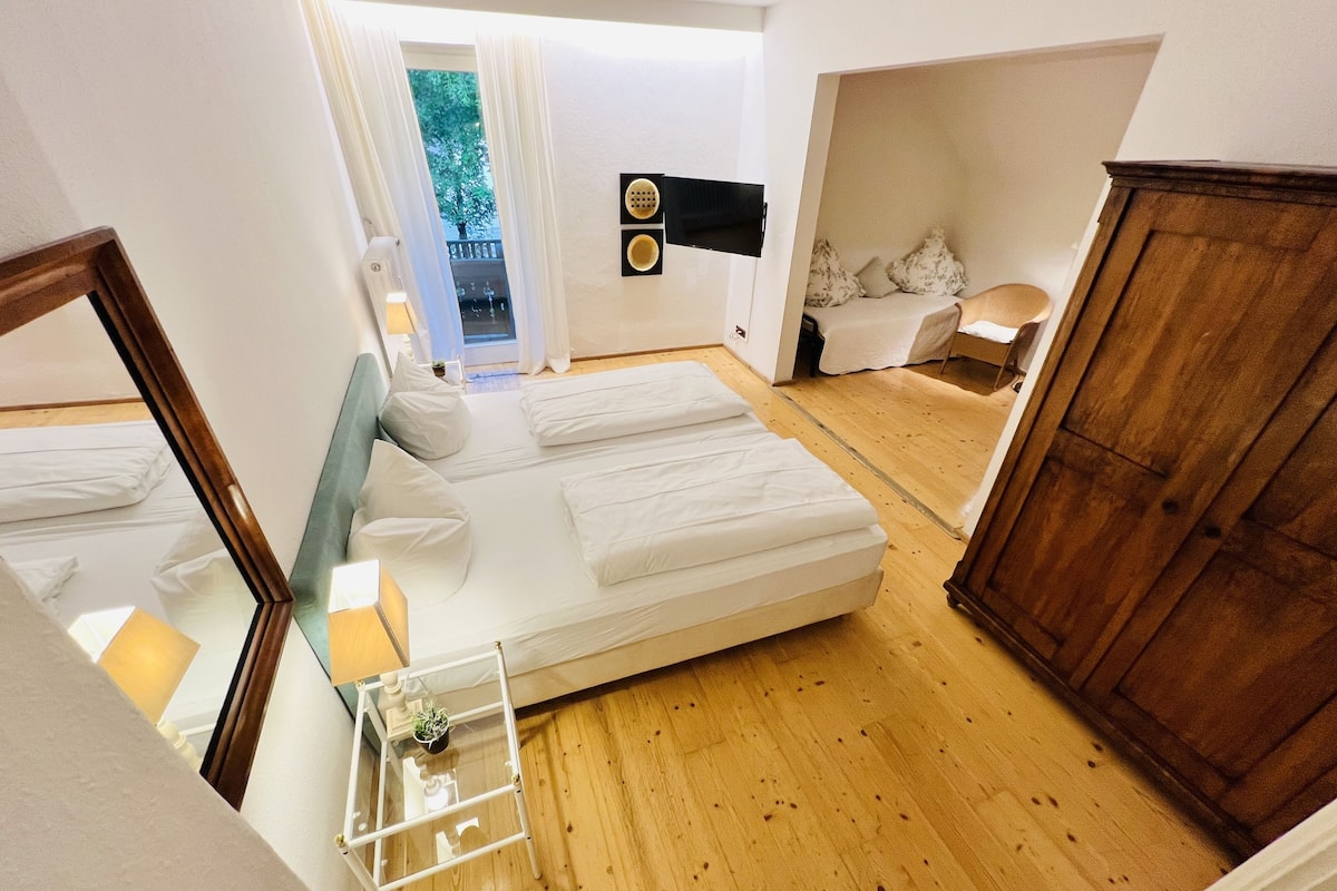 Ein Schlafzimmer mit zwei Betten, einem Holzschrank, einem Glastisch mit Pflanze und Blick ins Freie.